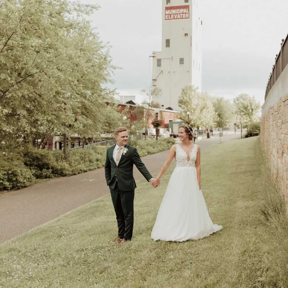 Bride and groom holding hands while walking in grass, City House Municipal Elevator in the backdrop