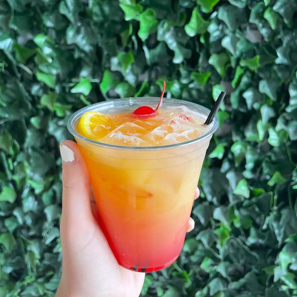 Tequila sunrise being held up by hand in front of ivy wall
