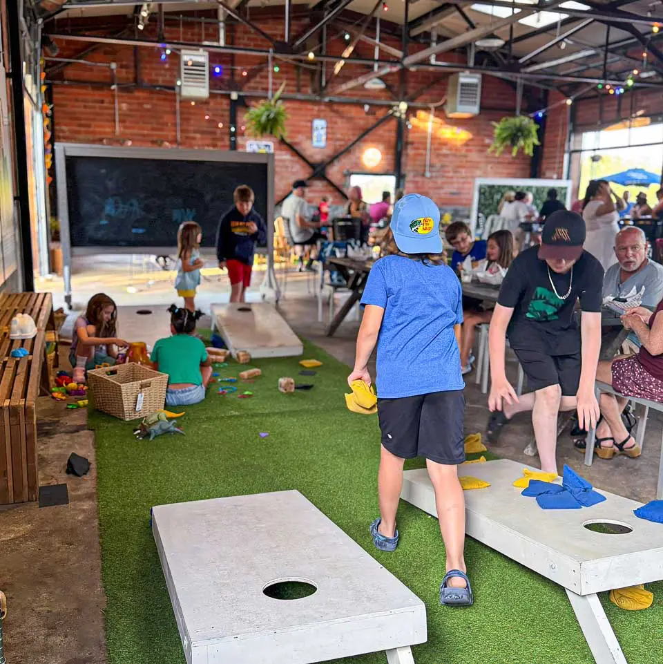 Children playing bean bag game as parent look on in brick building