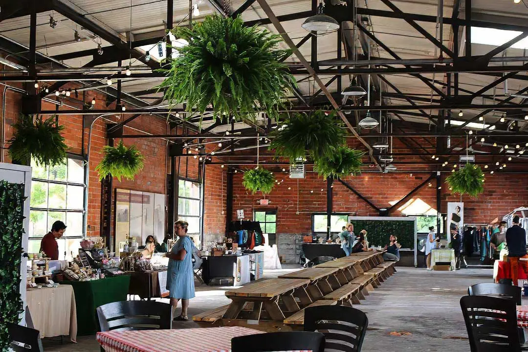 Ferns hanging from rafters inside City House, shoppers visiting with small market vendors